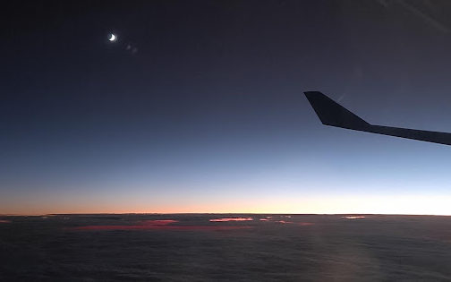 picture of a plane over clouds with the moon in the background